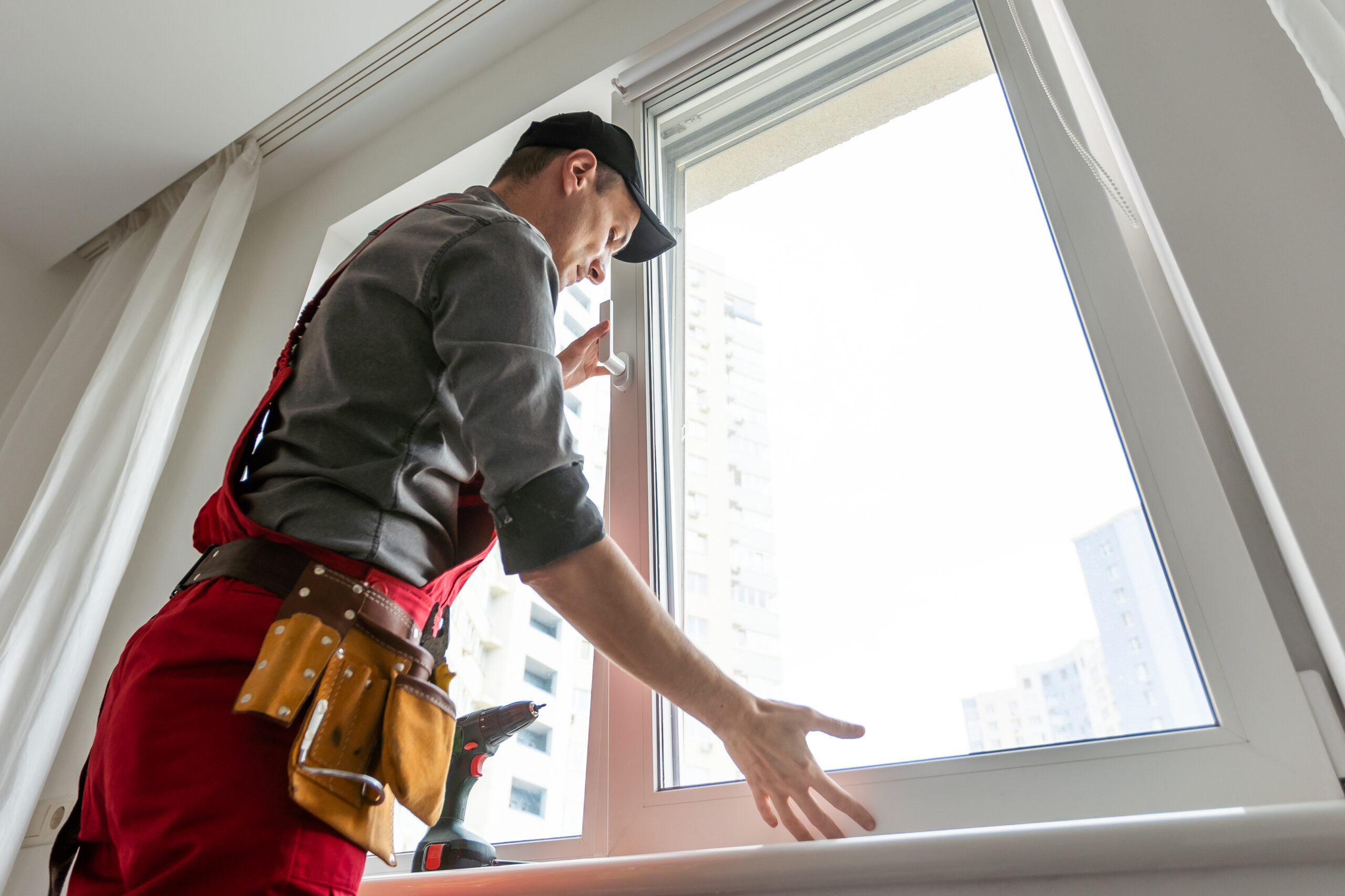 Workman in overalls installing or adjusting plastic windows in the living room at home